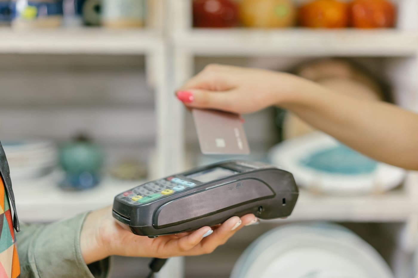 A hand tapping a credit card on a card reader at a checkout counter
